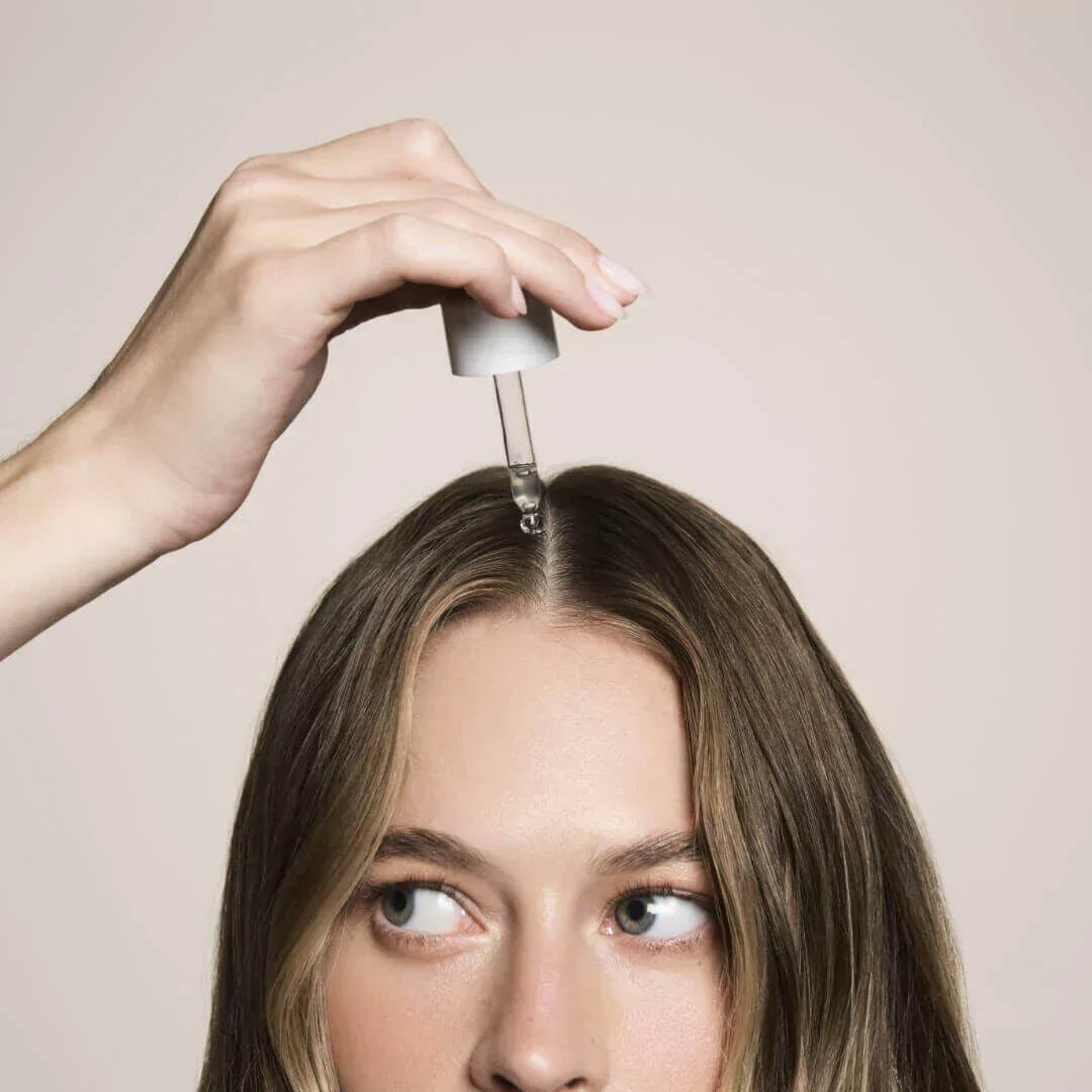 Woman placing actiiv thickening hair serum on her head with dropper