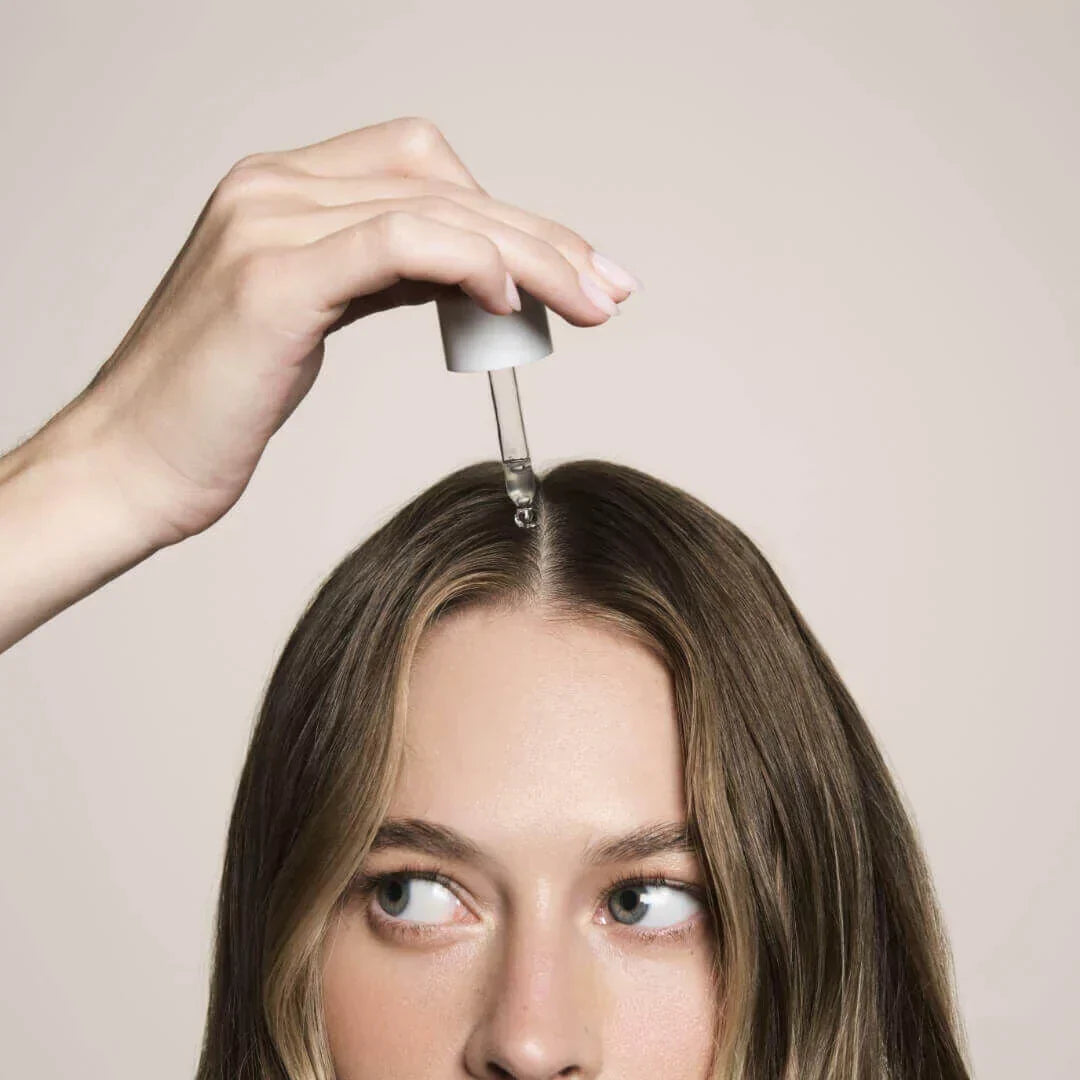 Woman placing actiiv thickening hair serum on her head with dropper