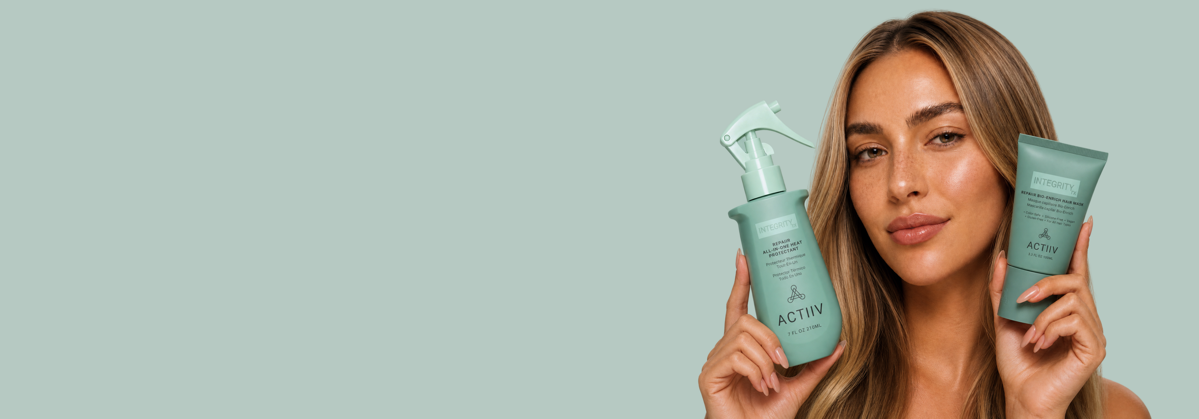 Woman holding ACTIIV INTEGRITYrx Repair Bio-Enrich Hair Mask and All-in-One Heat Protectant for damaged hair.