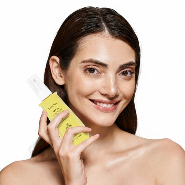 Woman holding a yellow bottle of Defense spf hair skin and scalp spray with a white background