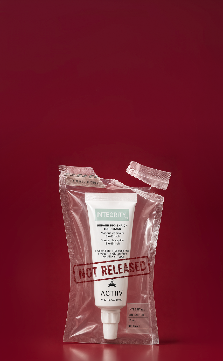 A tube of ACTIIV IntegrityRX Repaiir Hair Mask inside a clear plastic pouch with a torn top seal and a red 'NOT RELEASED' stamp, set against a solid dark red background.