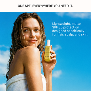 A smiling woman with wet hair wrapped in a white towel, holding a yellow bottle of ACTIIV Defense SPF 30 Hair, Scalp, and Skin Spray against a bright blue sky. Text reads: One SPF. Everywhere you need it. Lightweight, matte SPF 30 protection designed specifically for hair, scalp, and skin.