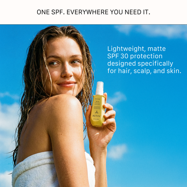 A smiling woman with wet hair wrapped in a white towel, holding a yellow bottle of ACTIIV Defense SPF 30 Hair, Scalp, and Skin Spray against a bright blue sky. Text reads: One SPF. Everywhere you need it. Lightweight, matte SPF 30 protection designed specifically for hair, scalp, and skin.