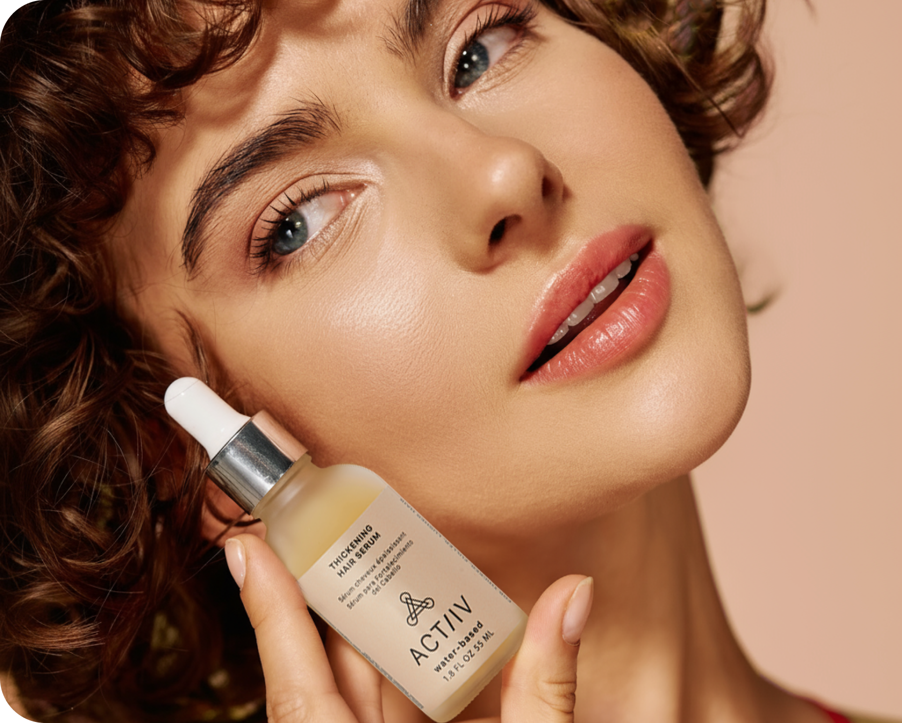 Woman holding a bottle of ACTIIV water-based thickening hairserum close to her face against a neutral background