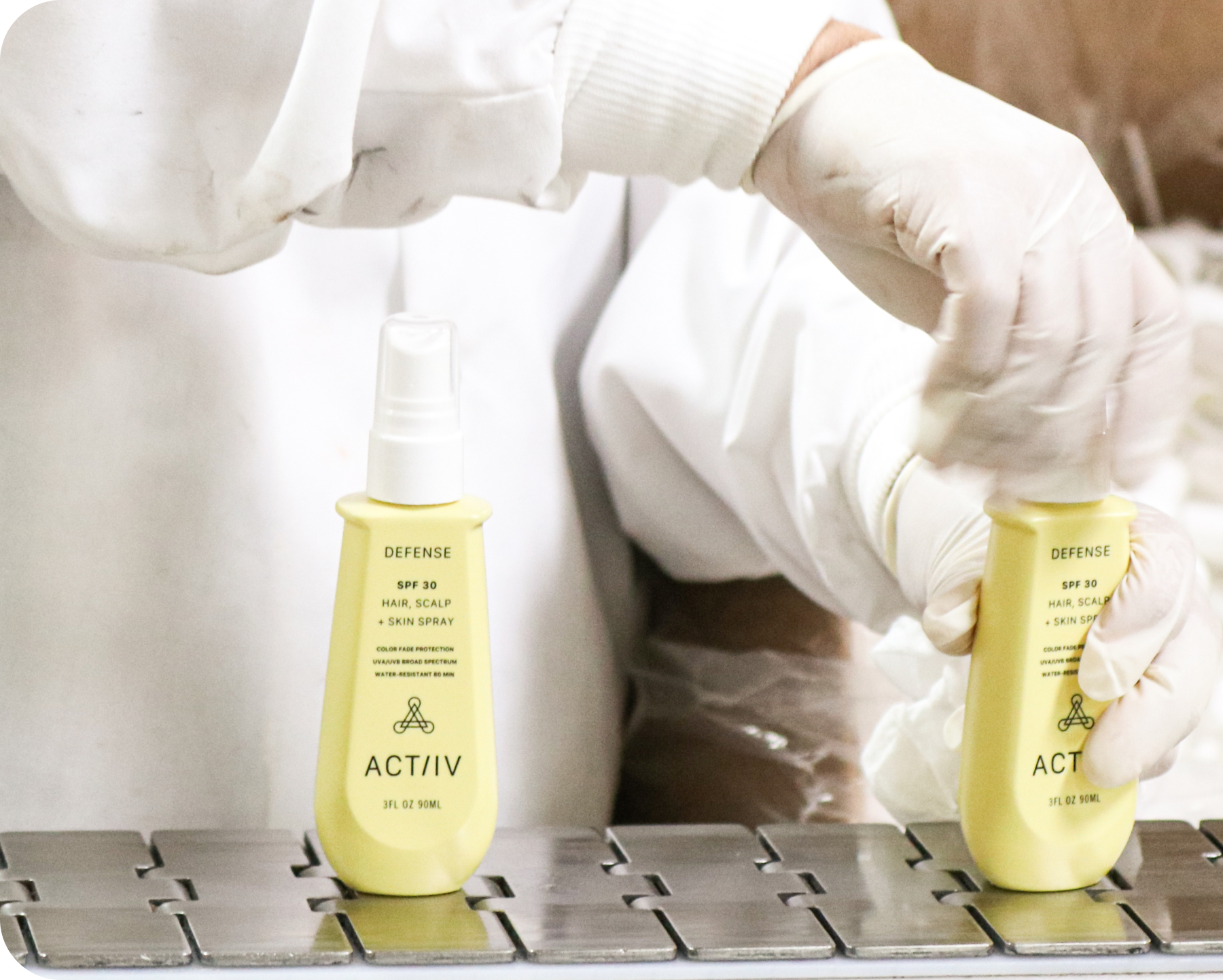 Person wearing gloves holding two bottles of ACTIIV defense SPF  product on a metal surface.