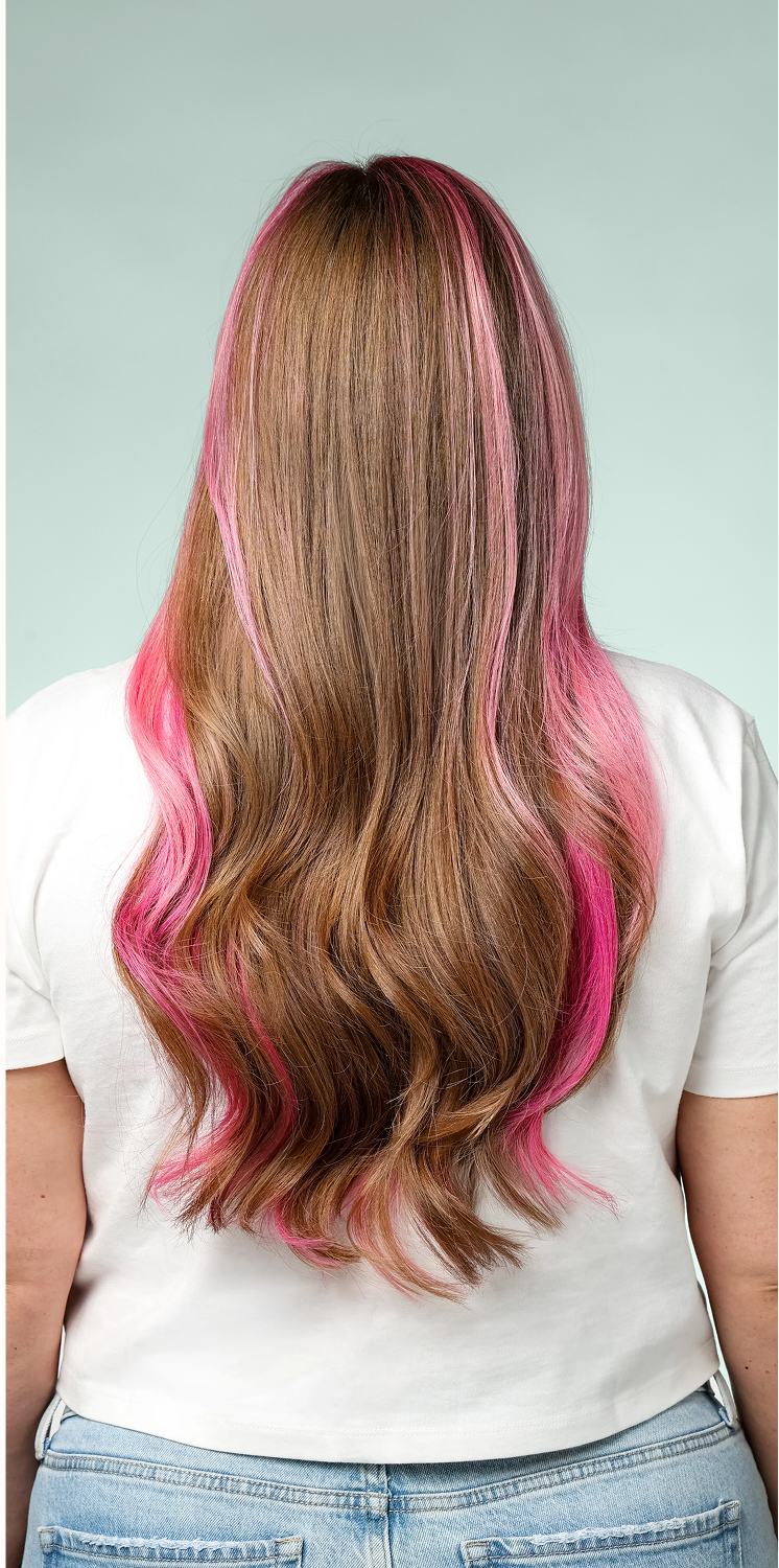 Long, smooth brown hair with vibrant pink highlights styled in glossy waves, showcasing shine, softness and a polished finish.