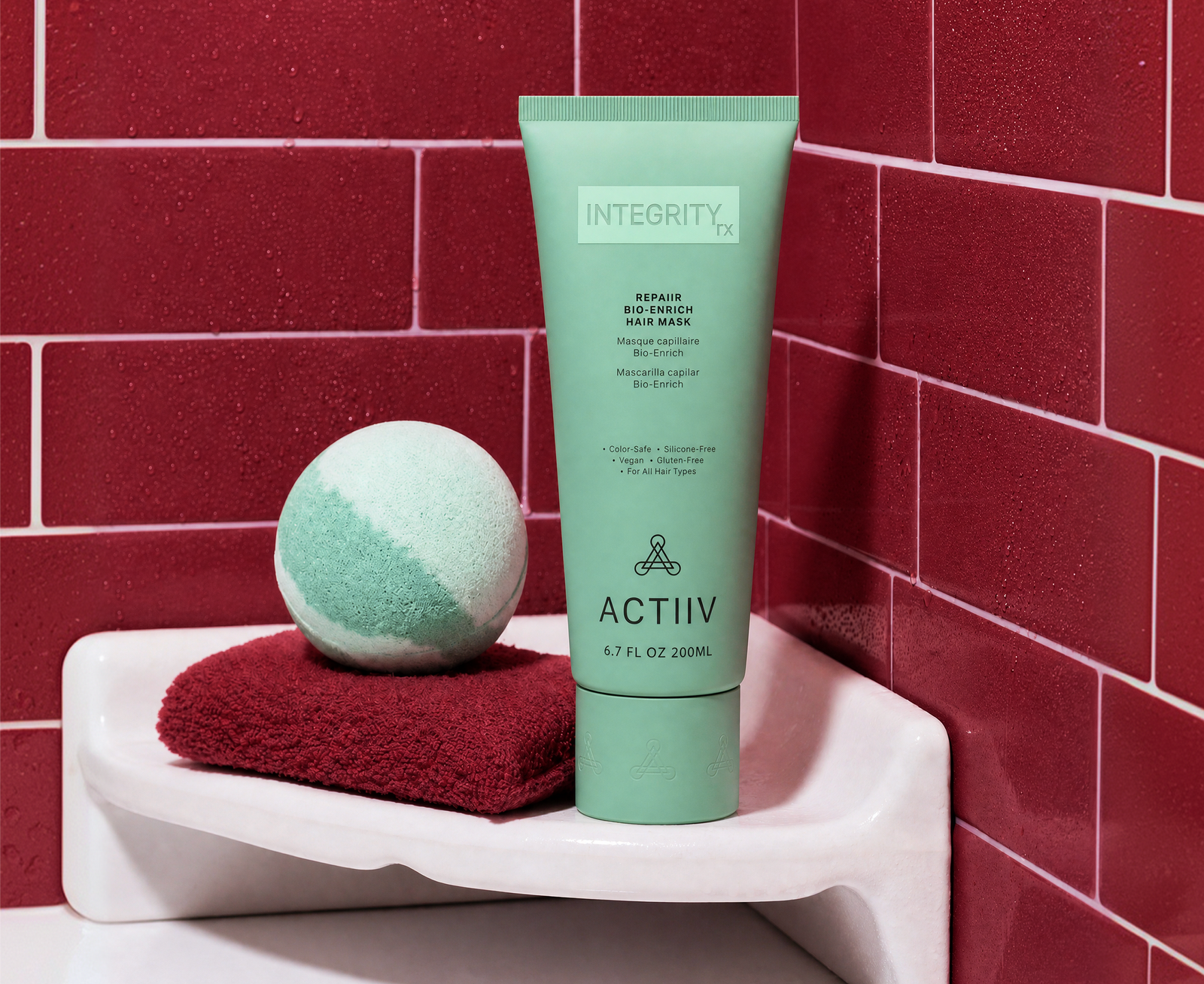 ACTIIV INTEGRITYrx Repair Bio-Enrich Hair Mask displayed in a red-tiled shower setting with a folded towel and bath accessory.